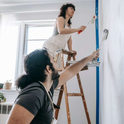 A couple painting a wall together with paint rollers.