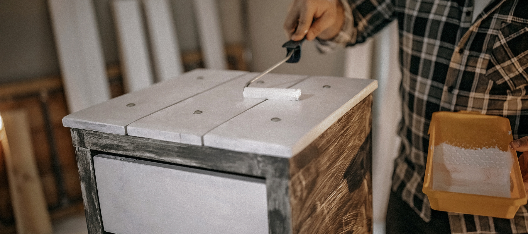 A small paint roller, painting wood with white paint.